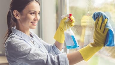 Frau putzt Fenster mit Lappen und Sprühflasche