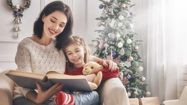 Mutter und Tochter lesen vor dem Weihnachtsbaum ein Buch zusammen