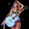 Taylor Swift mit Gitarre um den Bauch lächelt und fährt sich durch die Haare