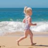 Blondes Mädchen rennt am Strand vor dem Meer rum und trägt einen Badeanzug