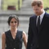 Prinz Harry sieht zu Boden, Herzogin Meghan läuft hinter ihm