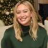 Hilary Duff sitzt lächelnd auf der Couch, im Hintergrund steht ein Weihnachtsbaum