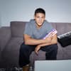 Emilio Sakraya sitzt auf einer Couch mit einer Tafel Milka in der Hand und einem Keyboard neben sich