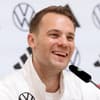 Manuel Neuer lacht in einer Trainingsjacke bei einer Pressekonferenz