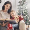 Mutter und Tochter lesen vor dem Weihnachtsbaum ein Buch zusammen