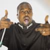 Kanye West mit Mikrofon und Fingerpistole.