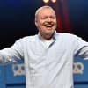 Stefan Raab lacht auf der Bühne und hält die Arme auf