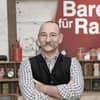  Horst Lichter mit verschränkten Armen vor dem "Bares für Rares"-Logo