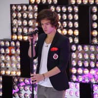 Harry Styles steht auf der Bühne und guckt ernst mit der Hand am Mikro 2012