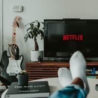 Füße liegen auf einem Couchtisch, davor steht ein Fernseher mit Netflix-Logo