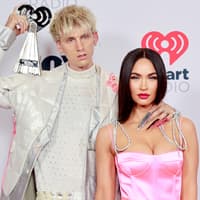 Machine Gun Kelly hält einen Award auf der Schulter, Megan Fox steht im rosanen Kleid neben ihm