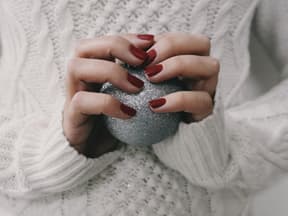 Frau mit rotem Nagellack hält silberne Kugel in der Hand