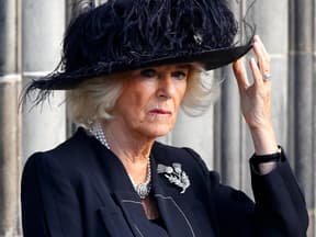 Queen Consort Camilla blickt ernst und fasst sich an den Hut