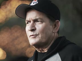 Charlie Sheen trägt eine Cap und einen Hoodie, sieht betroffen zur Seite