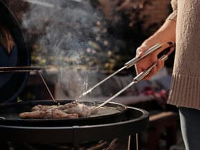 Frau grillt mit Grillzange in der Hand Hähnchen