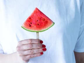 Rot lackierte Hand hält eine Wassermelone vor ein weißes Shirt