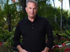 Kevin Costner lächelt leicht im Garten