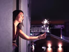 Frau hält Silvester allein eine Wunderkerze aus dem Fenster