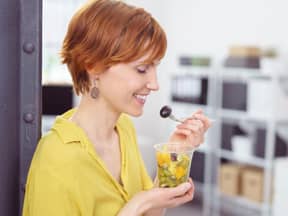 frau isst im büro einen gesunden obstsalat