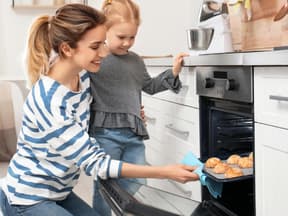 Mutter und Tochter öffnen Backofen mit Brötchen auf einem Backpapier Ersatz