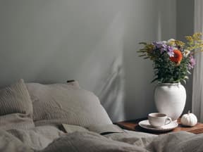 bett mit musselin bettwäsche dsneben blumen und kaffee