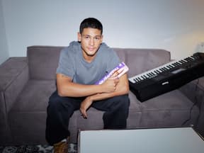 Emilio Sakraya sitzt auf einer Couch mit einer Tafel Milka in der Hand und einem Keyboard neben sich