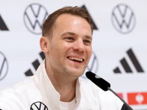 Manuel Neuer lacht in einer Trainingsjacke bei einer Pressekonferenz