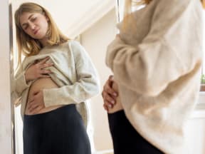 Frau schaut Bauch im Spiegel an