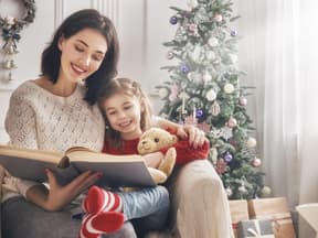 Mutter und Tochter lesen vor dem Weihnachtsbaum ein Buch zusammen