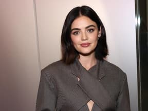 Lucy Hale steht vor einer Wand & guckt in die Kamera