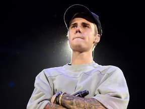 Justin Bieber steht mit verschränkten Armen und zusammengepressten Lippen da.