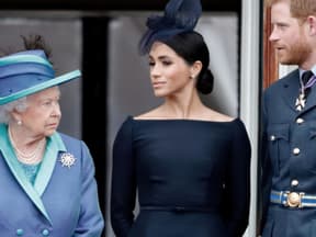 Die Queen, Meghan und Harry stehen nebeneinander und gucken ernst