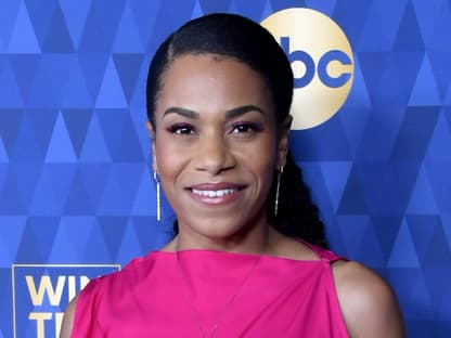 Kelly McCreary schaut lächelnd in die Kamera.