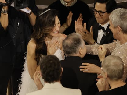 Michelle Yeoh legt die Hand auf die Brust und wird bejubelt und umarmt bei den Oscars 2023