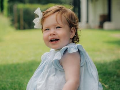 Prinzessin Lilibet sitzt in einem blauen Kleid auf dem Rasen und lacht