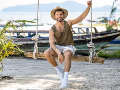 "Charming Boys"-Kandidat Martin Angelo lacht auf einer Schaukel am Strand