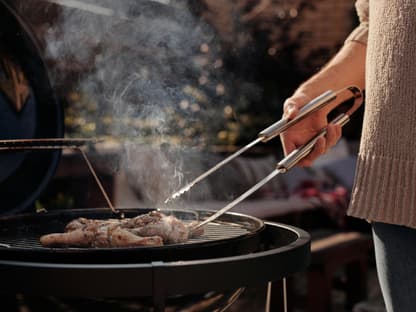 Frau grillt mit Grillzange in der Hand Hähnchen