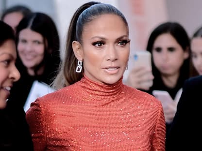 Jennifer Lopez geht in einem roten Glitzerkleid durch eine Menschenmenge