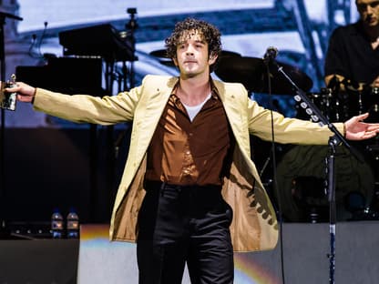 Matty Healy breitet die Arme auf der Bühne aus, in der Hand ein Flachmann