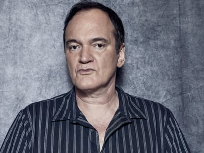 Quentin Tarantino trägt ein gestreiftes Hemd und sieht ernst in die Kamera