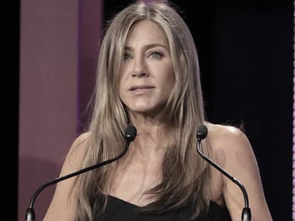 Jennifer Aniston steht mit traurigem Gesichtsausdruck am Mikrofon