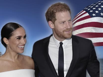 Herzogin Meghan und Prinz Harry vor USA-Flagge, beide lächeln.