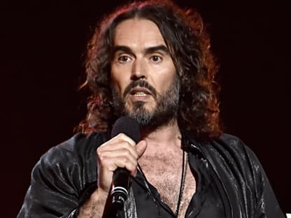 Russell Brand spricht ins Mikrofon und sieht verärgert aus