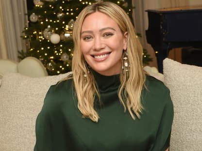 Hilary Duff sitzt lächelnd auf der Couch, im Hintergrund steht ein Weihnachtsbaum