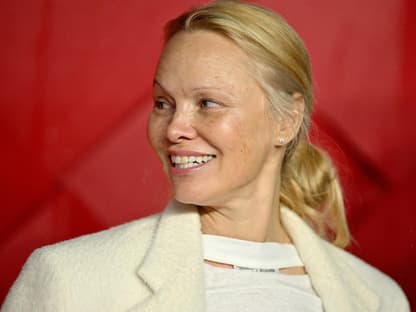 Pamela Anderson guckt zur seite und lächelt vor rotem Hintergrund