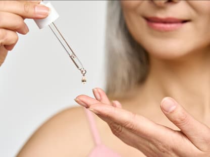 Frau mit Pipette gibt Anti-Aging-Serum auf Finger