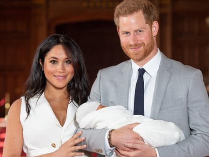 Harry und Meghan lächeln in die Kamera während Harry Archie hält.