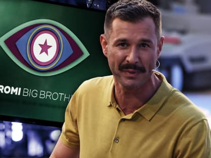 Jochen Schropp steht vor einem Promi Big Brother Bildschirm.