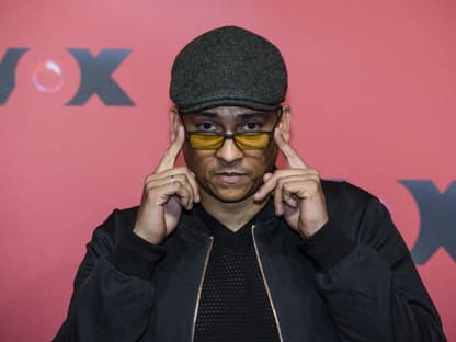 Xavier Naidoo hält mit den Händen seine Sonnenbrille und trägt eine Mütze