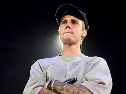 Justin Bieber steht mit verschränkten Armen und zusammengepressten Lippen da.